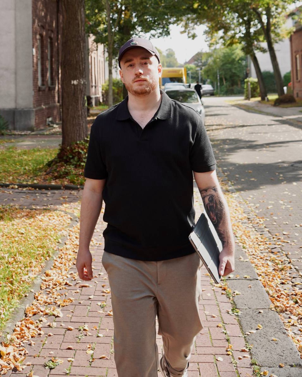 Yannick Breuer unterwegs in einer Wohnstraße, ein Tablet unter dem Arm